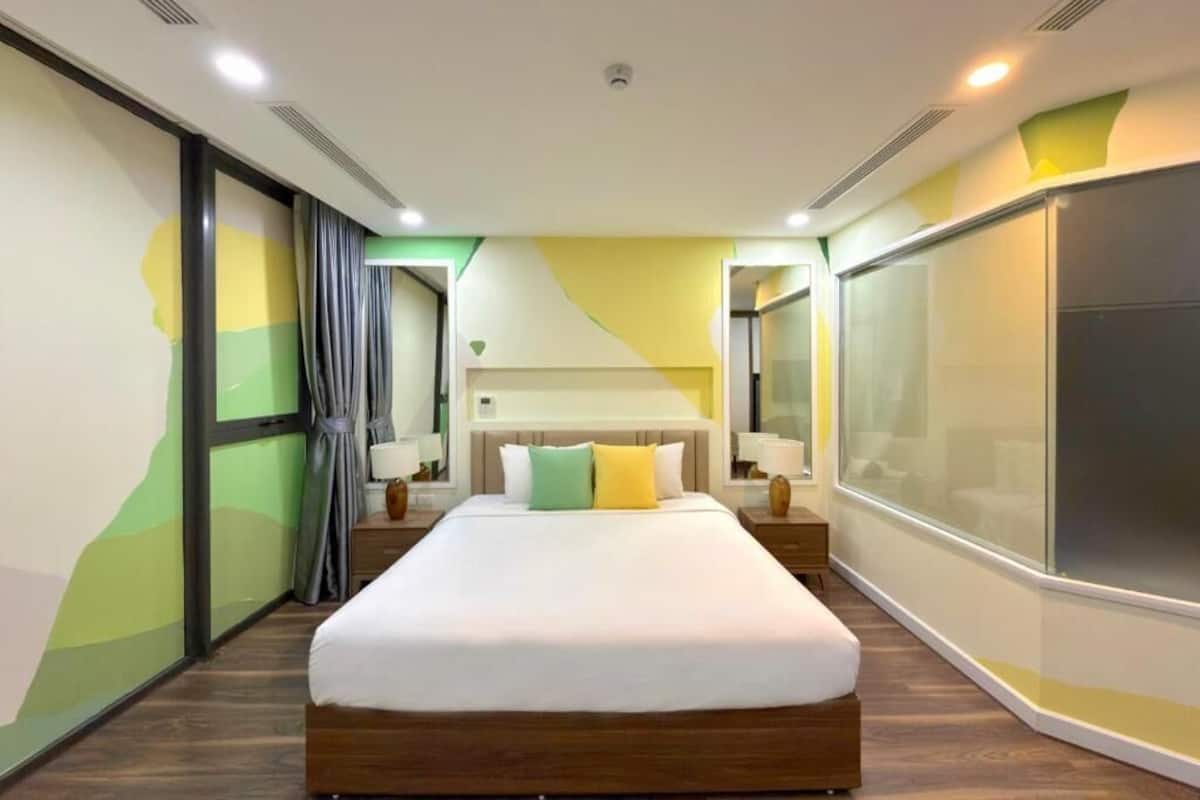 Una habitación de hotel moderna con una cama grande, mesitas de noche y un ventanal amplio.