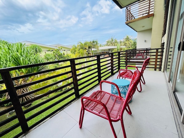 A balcony with red wicker furniture, a small table, and a view of a garden with a pond. - Costa Pacifica Baler (Baler)