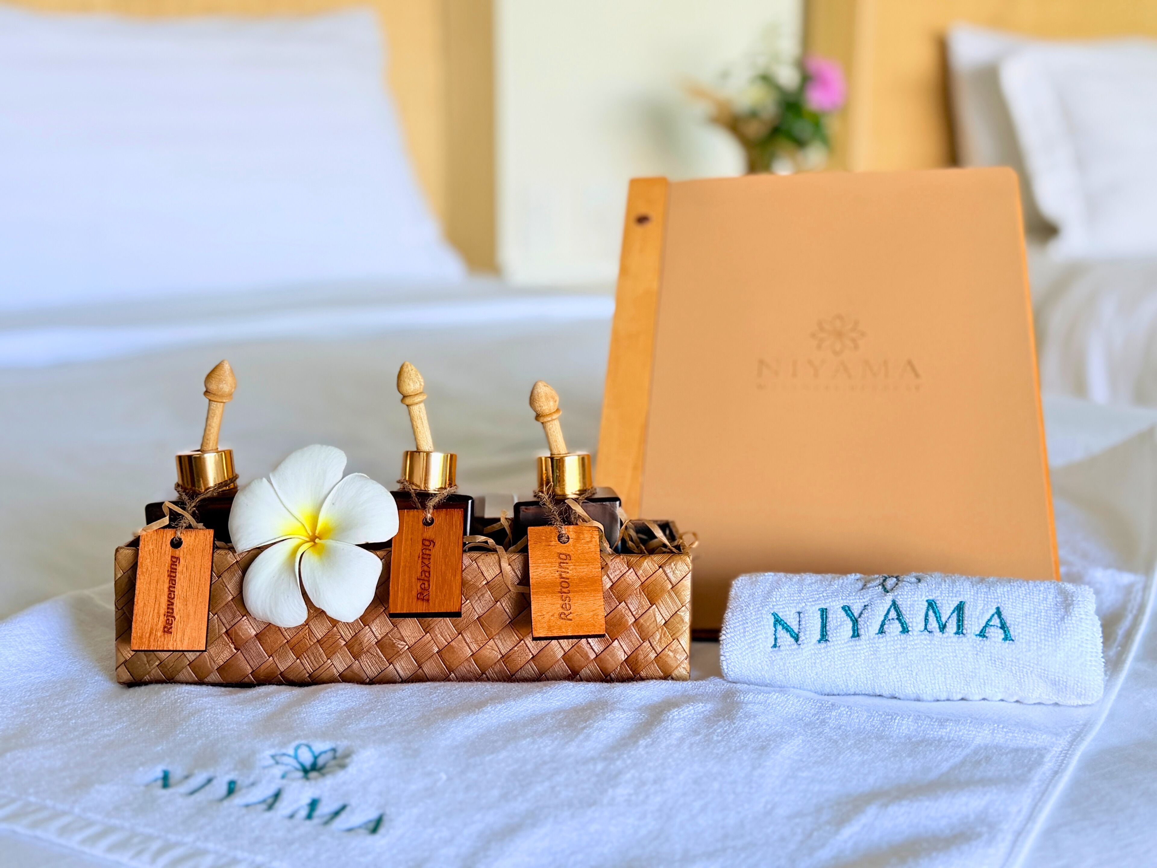 Un conjunto ordenado de herramientas de masaje de madera sobre una cama con una toalla blanca con la etiqueta 'NIYAMA' y una bolsa con el logo de la marca al fondo.