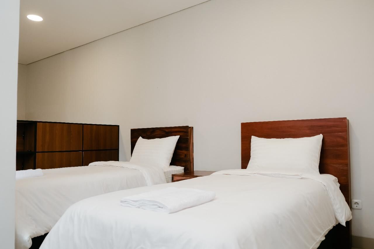 Habitación de hotel con dos camas individuales, cabeceros de madera, ropa de cama blanca y una lámpara empotrada en el techo.
