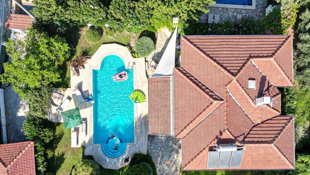 Ovenfra set et ejendom med swimmingpool, stenskikkede stier og et hus med rødt tegltag.