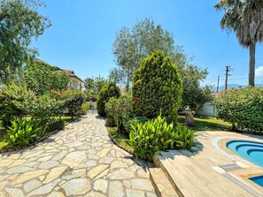 Ein Steinweg führt zu einem Poolbereich mit üppiger Bepflanzung und einem gepflegten Garten.