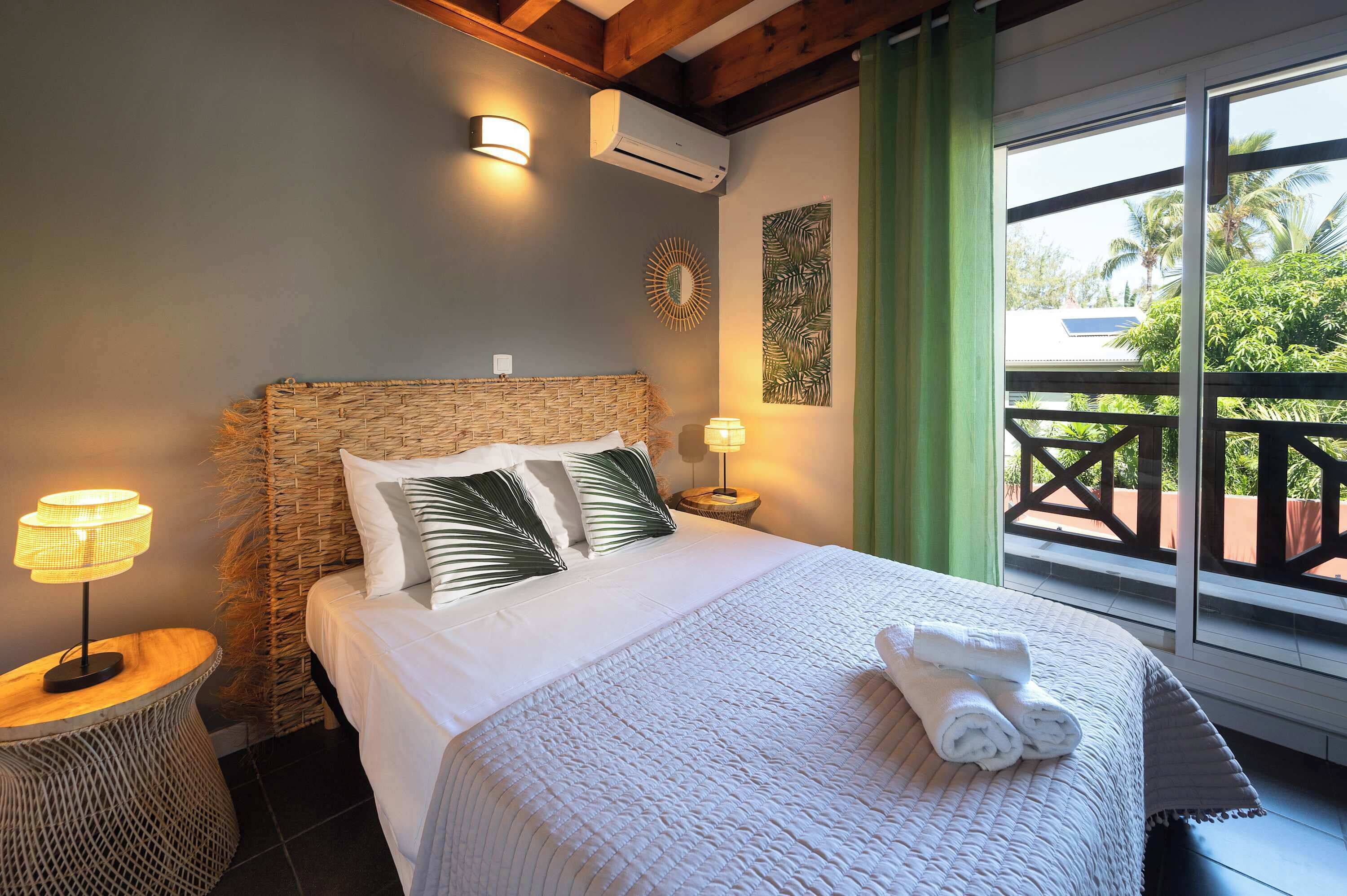 A bedroom with a bed, a nightstand, a wall-mounted air conditioner, and a view of the outdoors.