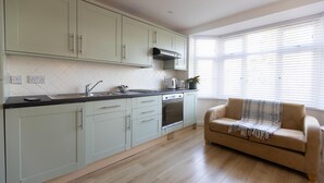 A modern kitchen with light green cabinets, a black countertop, and a beige sofa near a large window.
