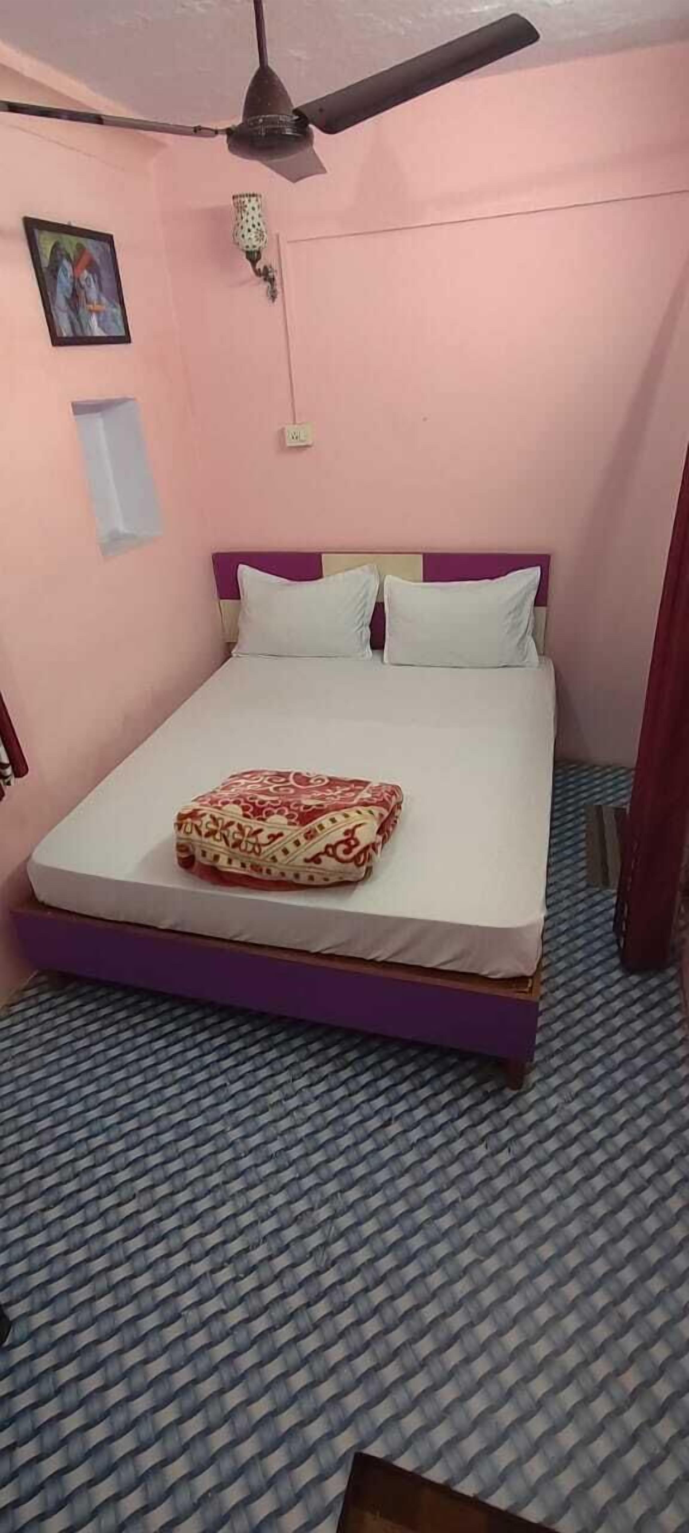 A single bed with a purple frame and white bedding, a ceiling fan, a wall-mounted light fixture, and a framed picture on the wall.