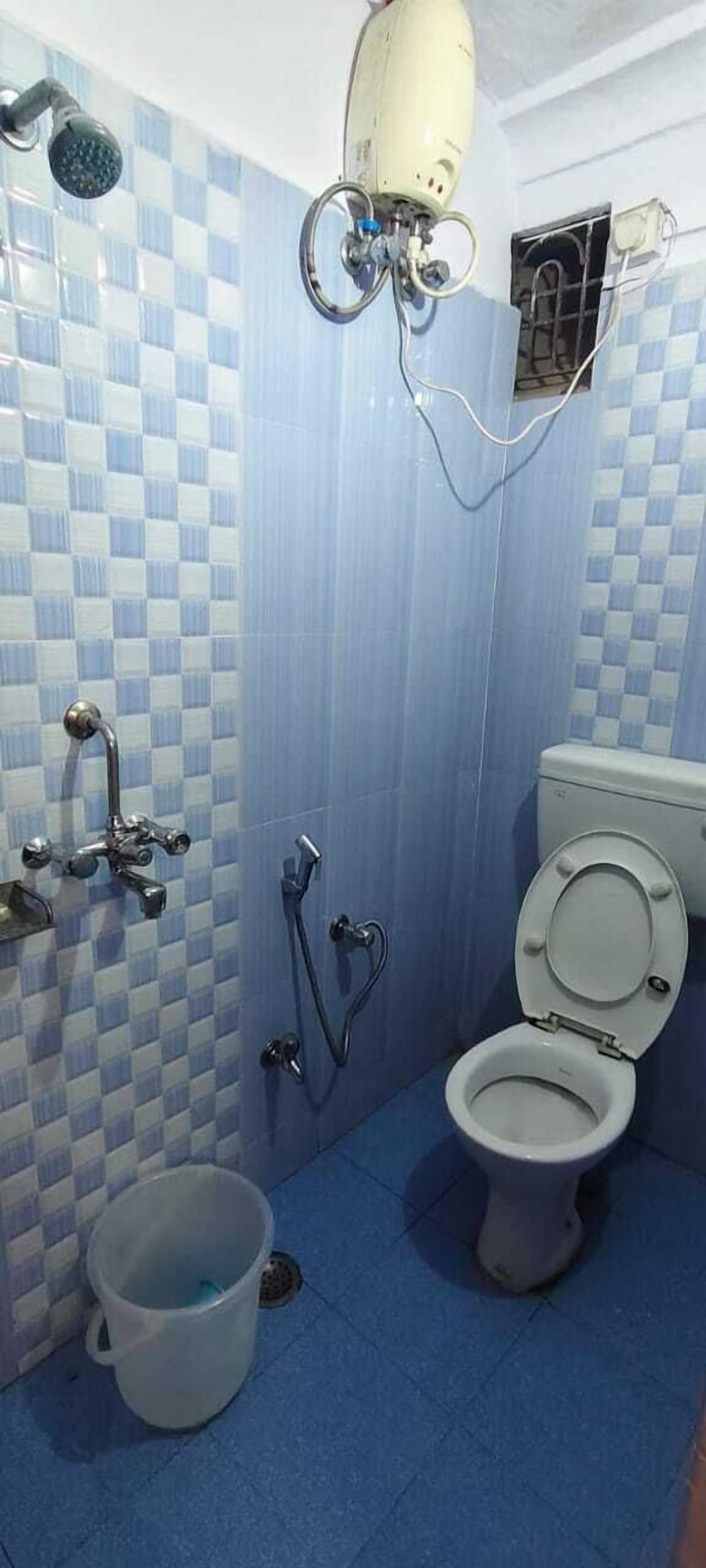 Kylpyhuoneessa on sinivalkoruudullinen laattaseinä, valkoinen wc-istuin, suihkupää ja lattialla ämpäri.