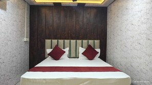 Un lit avec une tête de lit en bois, deux oreillers et une couverture rouge.