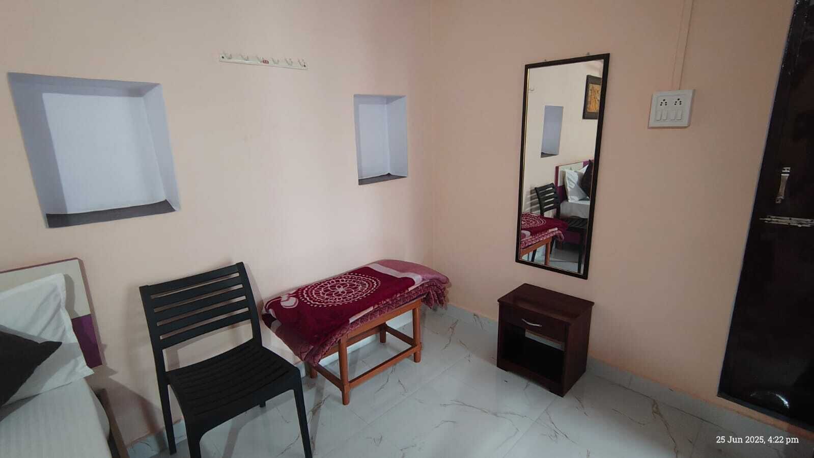 Una habitación pequeña y sencilla, con cama, silla, mesita de noche, espejo y un armario pequeño.