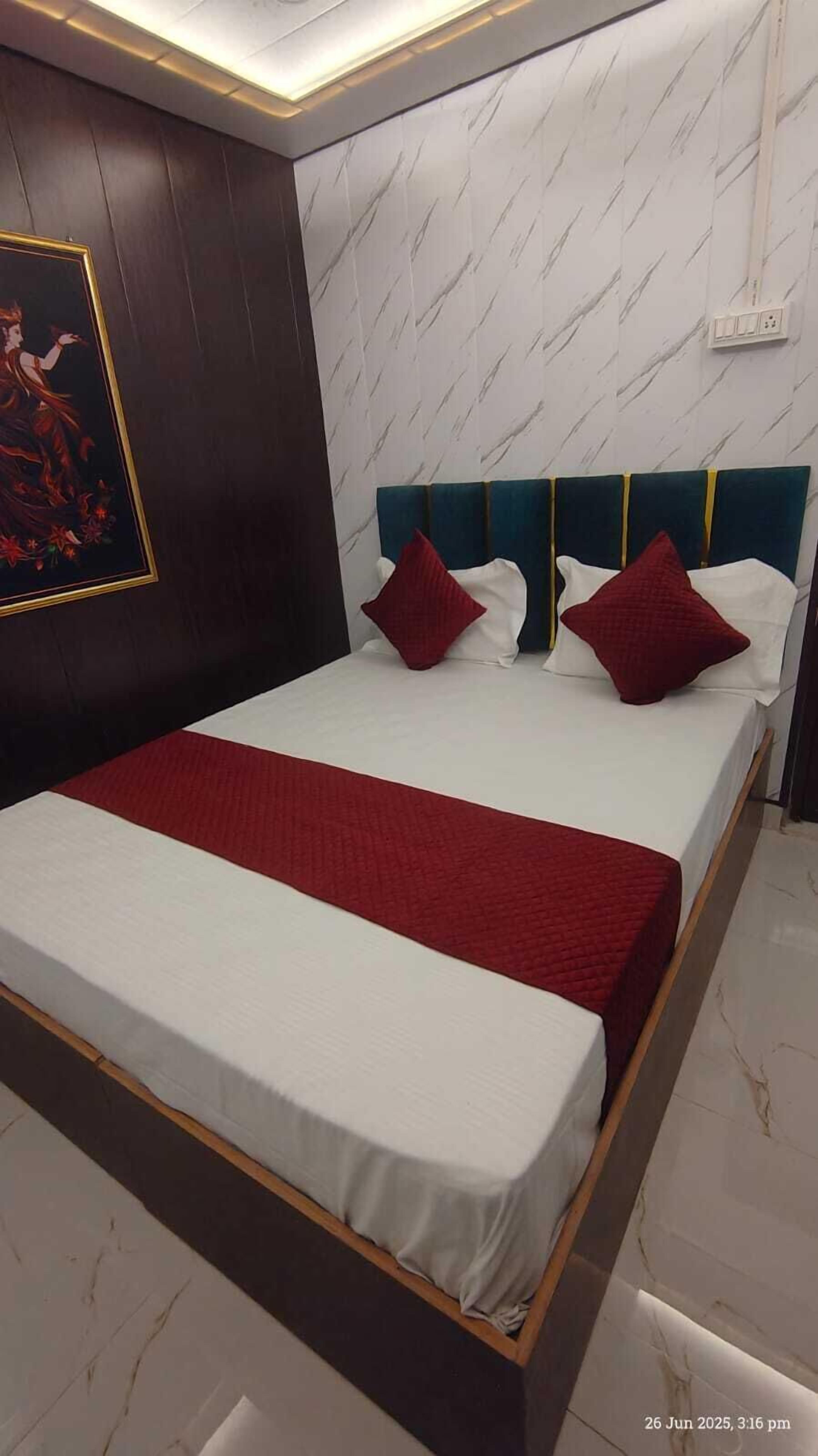 Ein ordentlich bezogenes Bett mit roter Decke und Kissen, ein dunkles Kopfteil und eine Wand mit Marmoroptik.