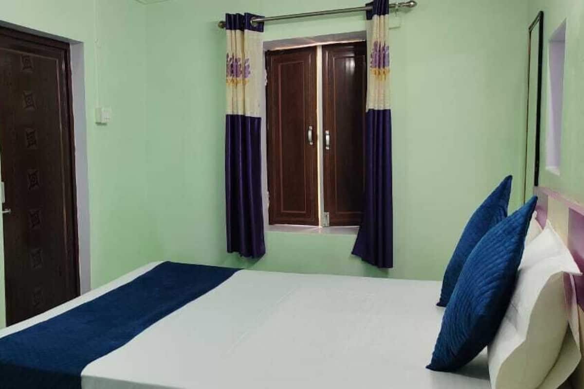 Une chambre à coucher avec un lit, une fenêtre avec des rideaux, une porte et une prise de courant.
