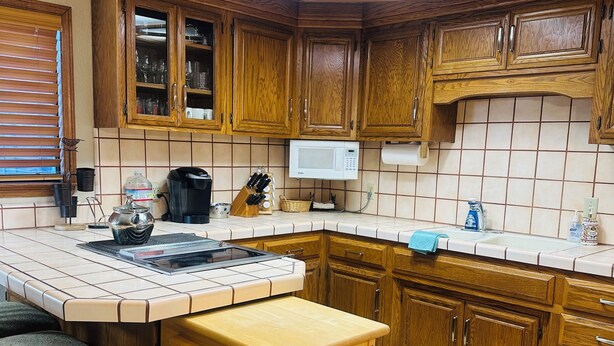 A kitchen with wooden cabinets, a microwave, and a large island with a sink. - Soothing cottage in the heart of Silicon Valley. (Santa Clara)