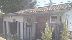 A house with a tiled roof, a gated entrance, and a small garden with plants and a red flower. - Soothing cottage in the heart of Silicon Valley. (Santa Clara)