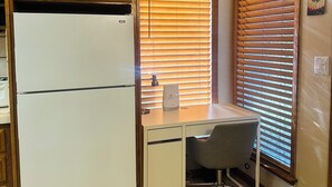 A kitchen with wooden cabinets, a white refrigerator, a built-in desk with a chair, and a window with blinds. - Soothing cottage in the heart of Silicon Valley. (Santa Clara)