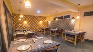 Un espace repas avec plusieurs tables dressées pour les repas, agrémenté d’un mur à motifs et de luminaires suspendus.