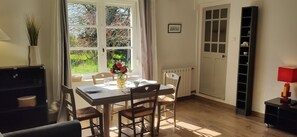 Un coin repas avec une table dressée pour deux personnes, un vase rempli de fleurs et une fenêtre donnant sur un paysage verdoyant.