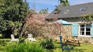 Ein Haus aus Stein mit einem geneigten Dach, einem Holztisch und zwei Stühlen.