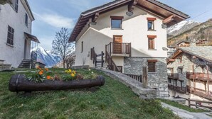 A two-story chalet with a stone facade, wooden balcony, and a log planter with flowers. - Maison du Chateau (La Salle)
