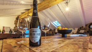 A bottle of Grosjean Mas Du Jario wine on a wooden table with two empty wine glasses, a bowl of fruit, and a book in a rustic setting with stone walls and wooden beams. - Maison du Chateau (La Salle)
