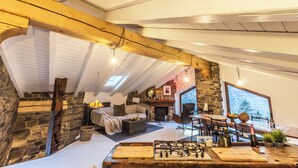 A cozy living room with a fireplace, stone walls, and a dining area with a wooden table and chairs. - Maison du Chateau (La Salle)