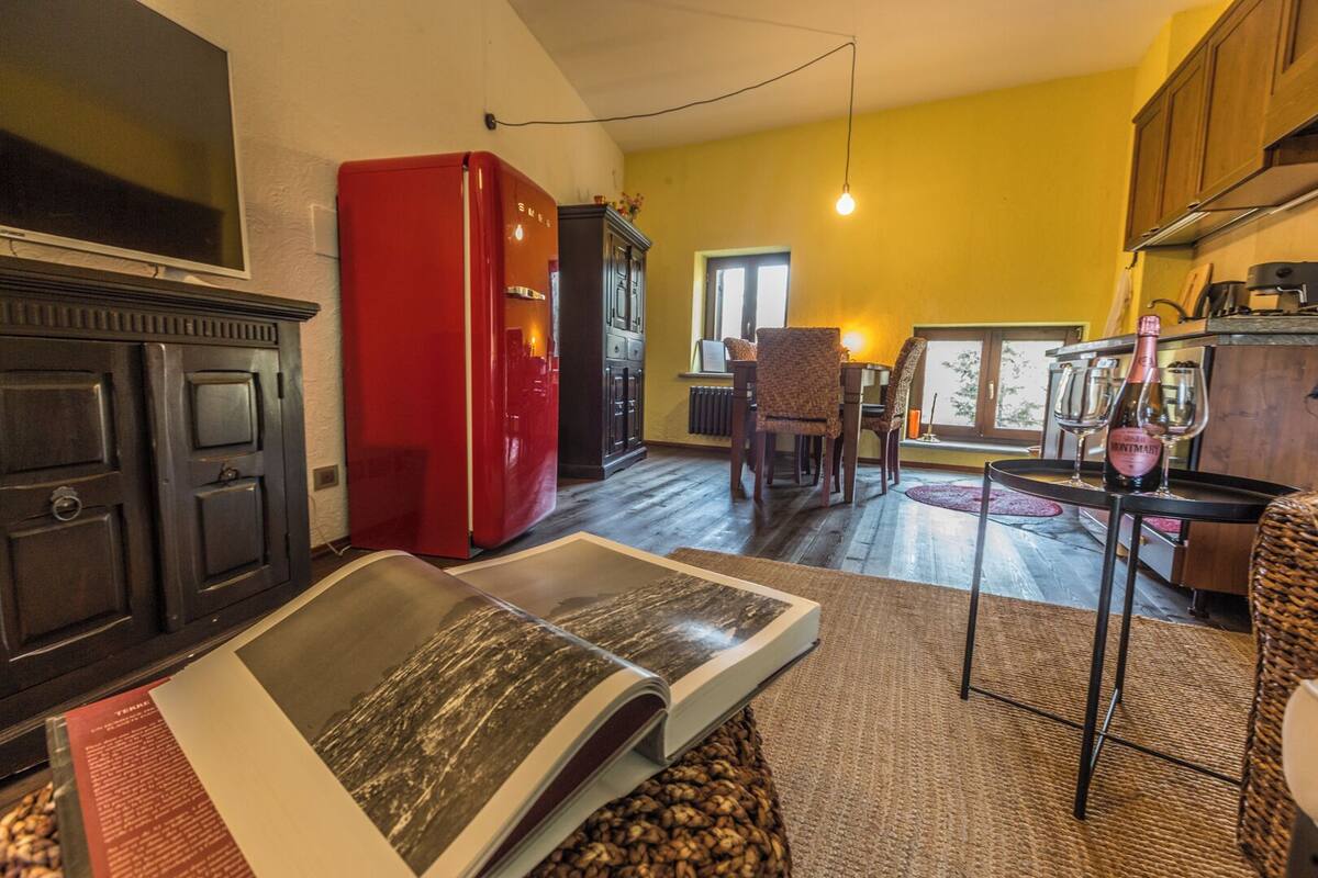 Een woonkamer met een rode koelkast, een zithoek met stoelen, een tafel met een fles wijn, en een groot boek op een salontafel.