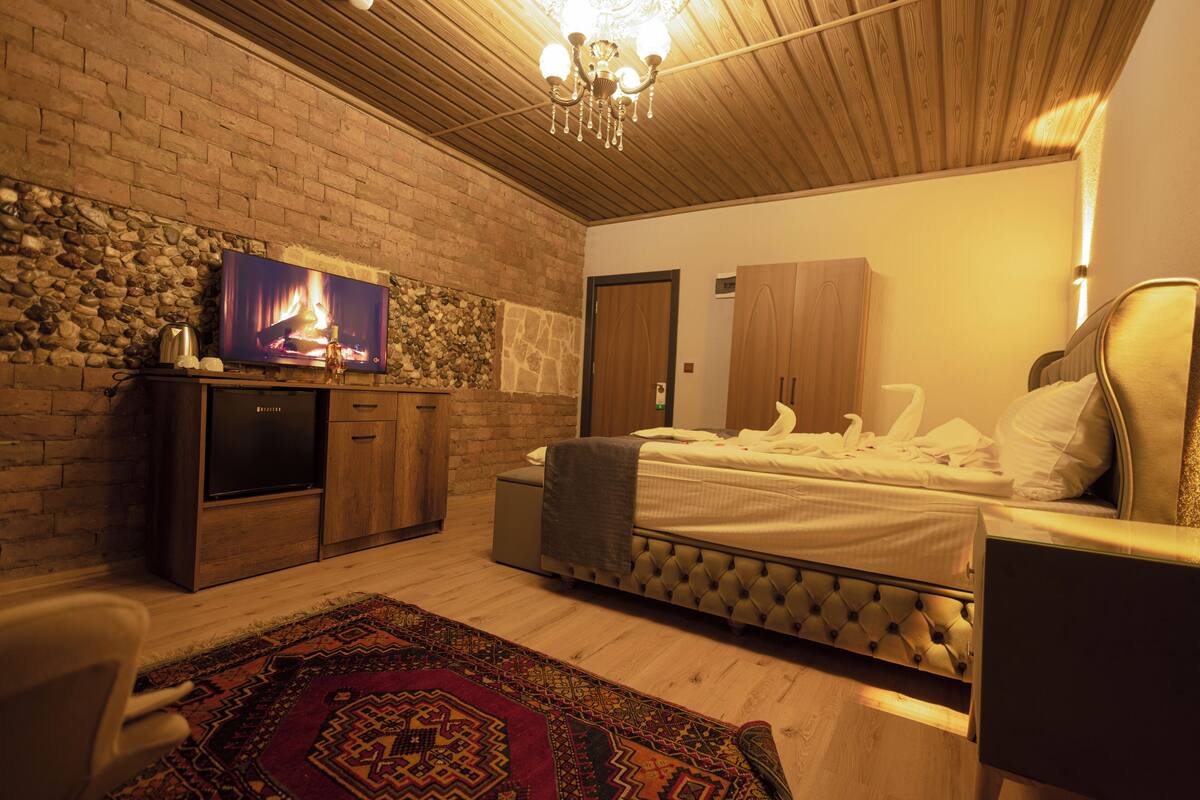 A bedroom with a stone wall, a television, a bed, and a wooden ceiling.