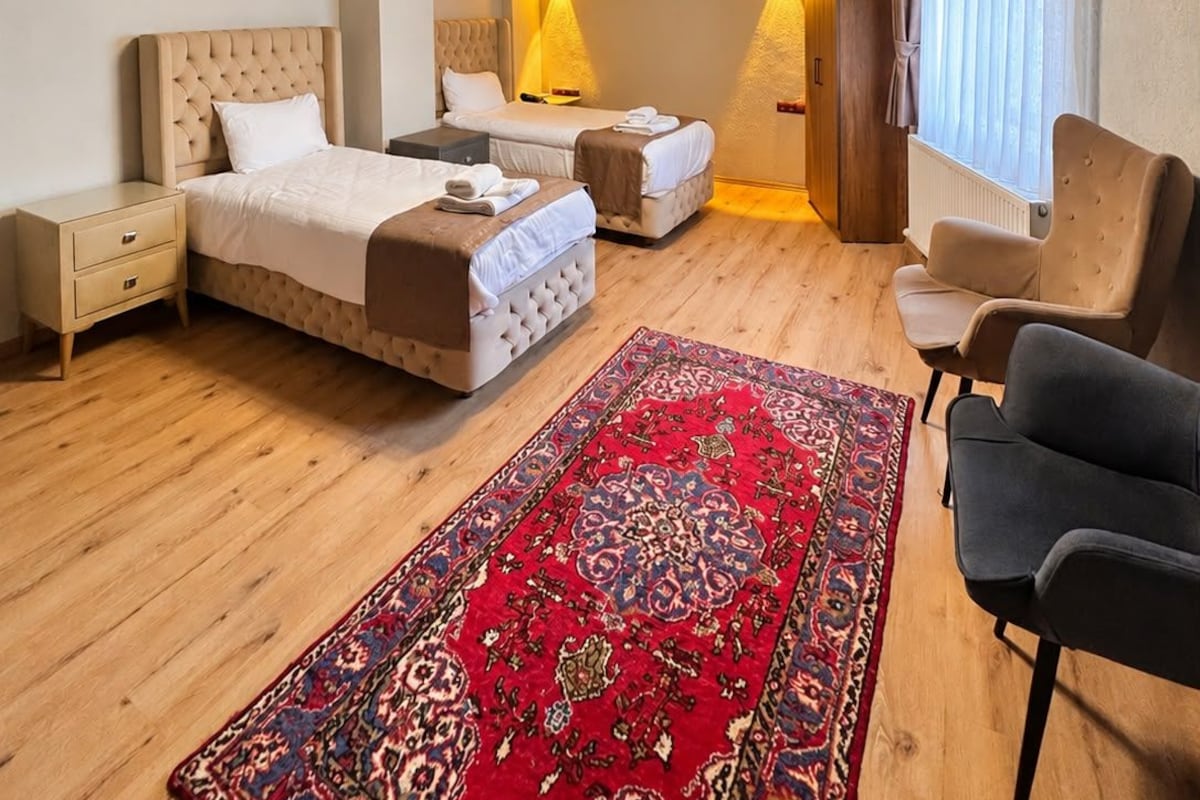 A hotel room with a wooden ceiling, a chandelier, a bed, a sofa, a chair, a nightstand, and a patterned rug.