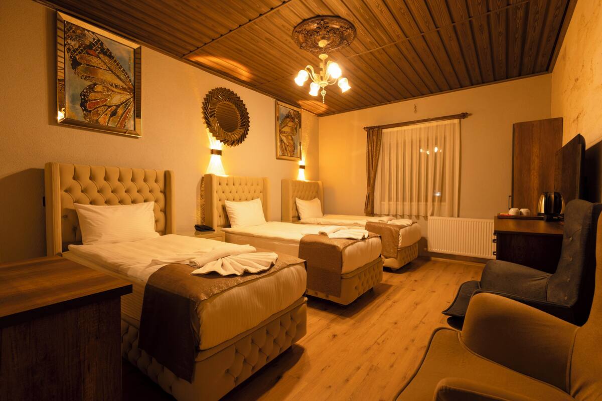 A hotel room with two beds, a sofa, a chair, a wooden ceiling, and artwork on the walls.
