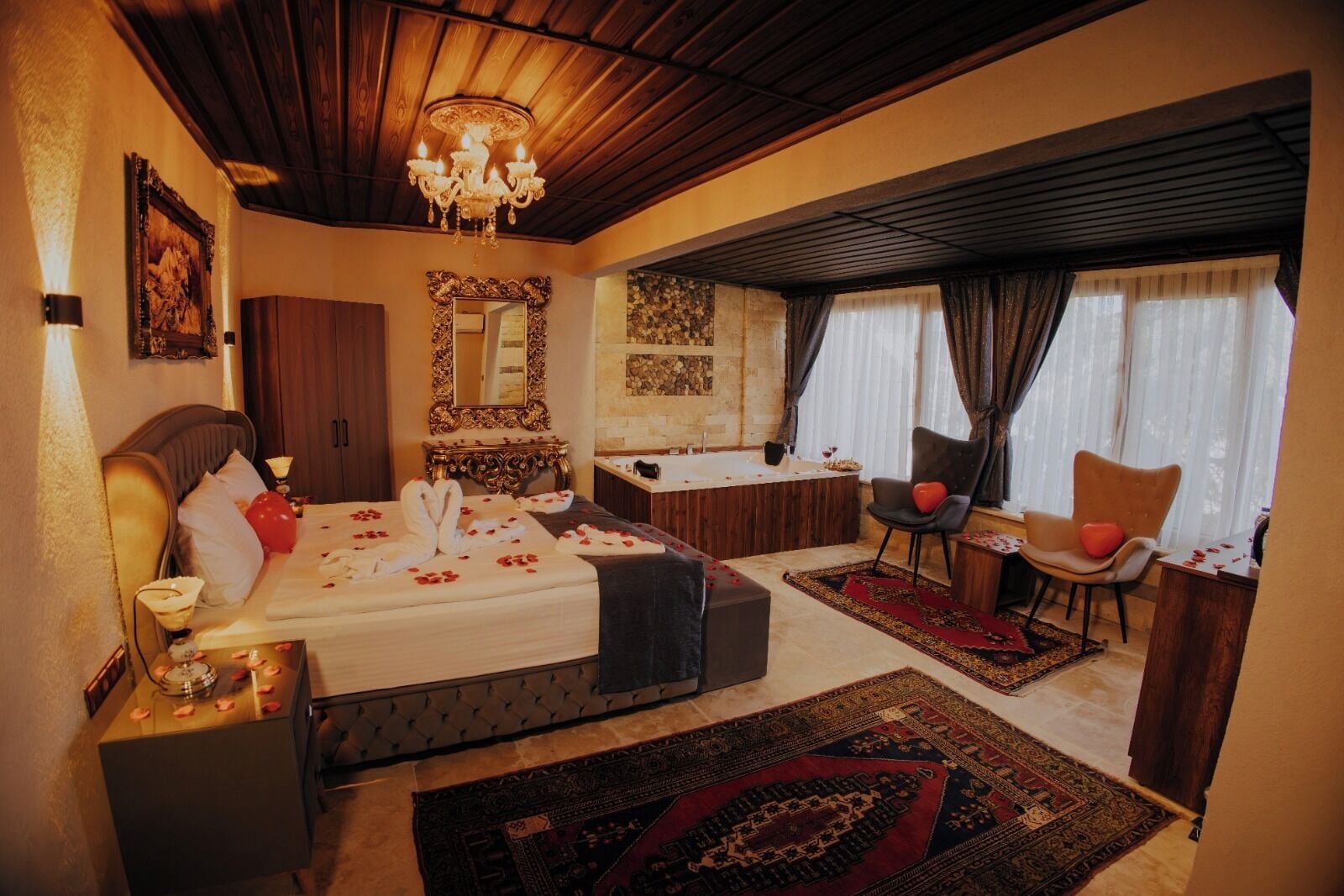 Habitación de hotel con cama, zona de estar con una silla, una mesita, bañera y un espejo grande.