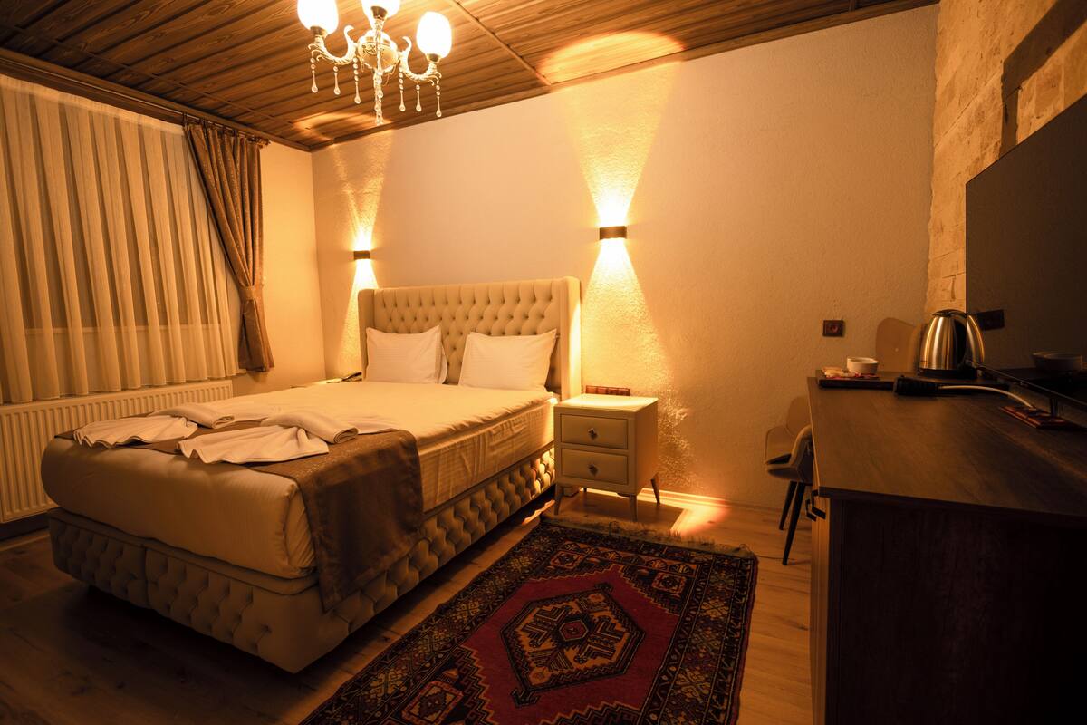 A bedroom with a large bed, bedside tables, a desk, and a chandelier.