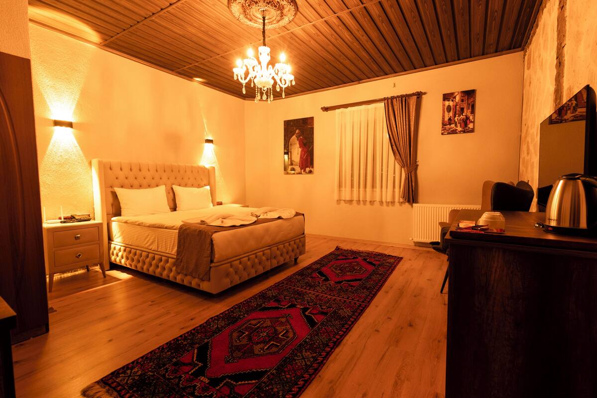 A bedroom with a bed, bedside table, lamp, chandelier, curtains, and a radiator.