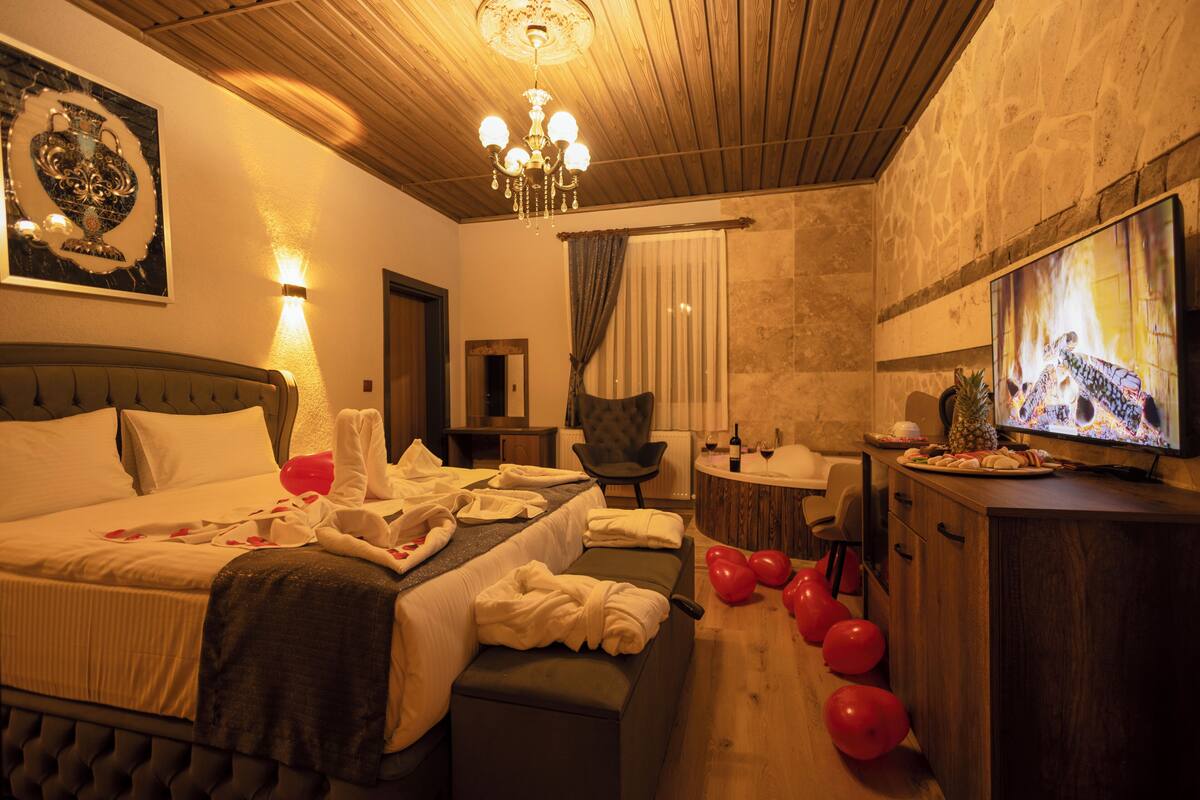 A hotel room with a bed, a sitting area, a television, and a minibar.