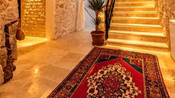 A stone-walled interior with a chandelier, a patterned rug, and a staircase.