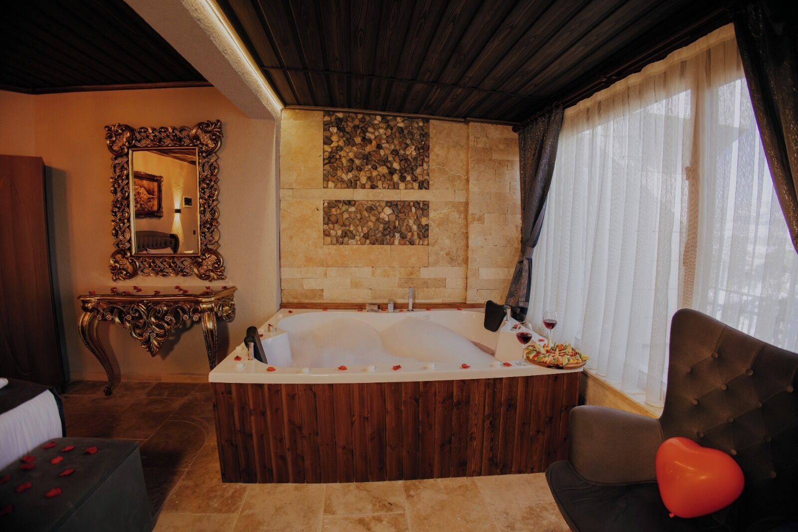 Une salle de bain avec une grande baignoire, un miroir, une console et une fenêtre avec des rideaux.