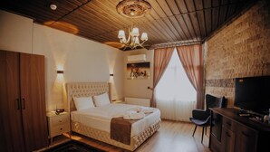 A hotel room with a large bed, a television, a desk, and a chair. - Konak Stone House (Urgup)