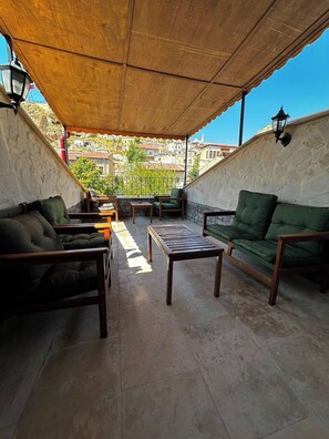 Eine Terrasse im Freien mit einem Holztisch und zwei Sofas, einer Steinmauer und Blick auf Gebäude im Hintergrund.