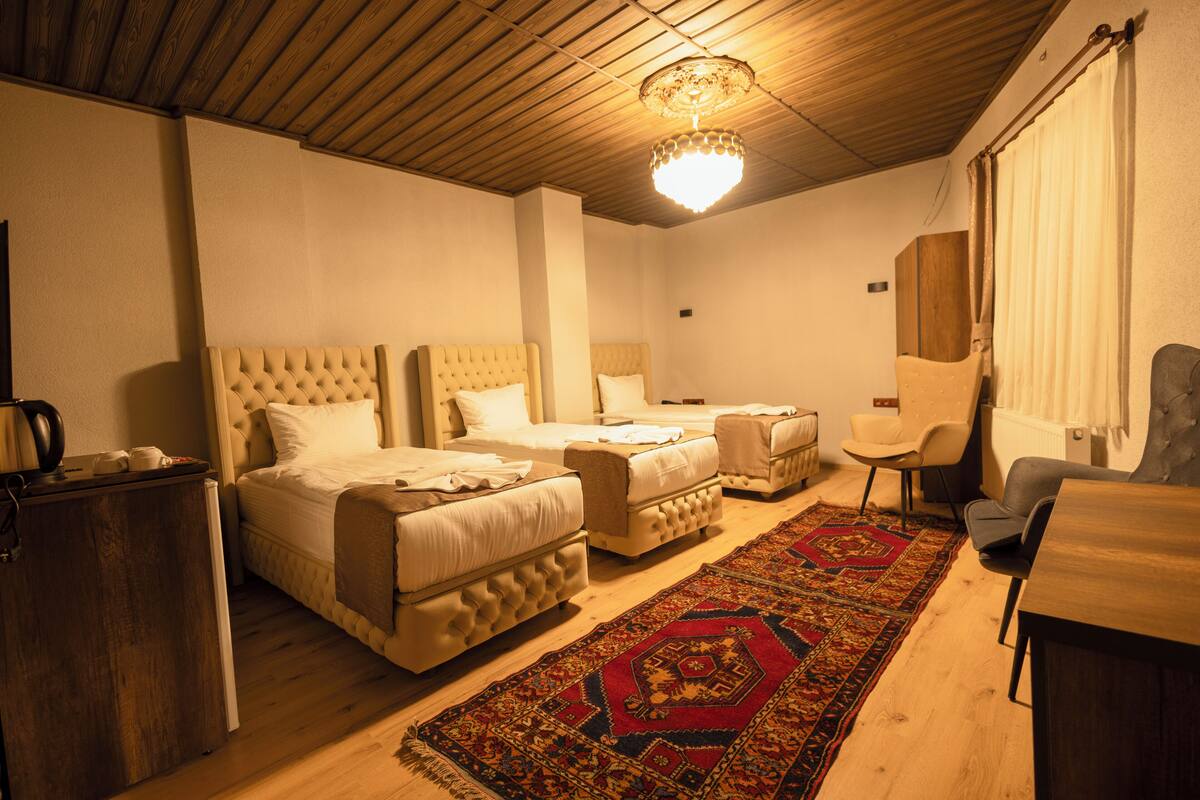 A hotel room with two beds, a wooden ceiling, a chandelier, a red and black patterned rug, and a small table.