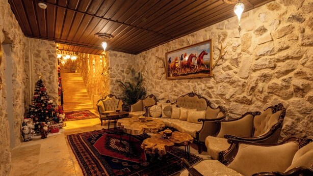 A cozy room with a stone wall, a fireplace, a Christmas tree, and a sofa set. - Konak Stone House (Urgup)