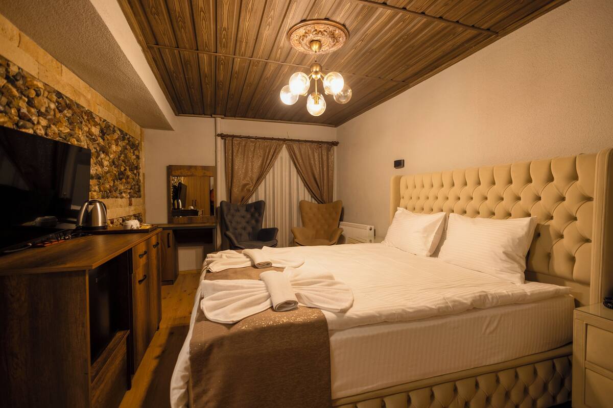 A hotel room with a large bed, wooden ceiling, a television, and a stone wall.