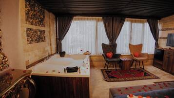 A room with a large bathtub, two chairs with heart-shaped cushions, a wooden cabinet, and a television.