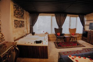 Ein Zimmer mit einer großen Badewanne, zwei Sessel mit herzförmigen Kissen, einem Holzschrank und einem Fernseher.