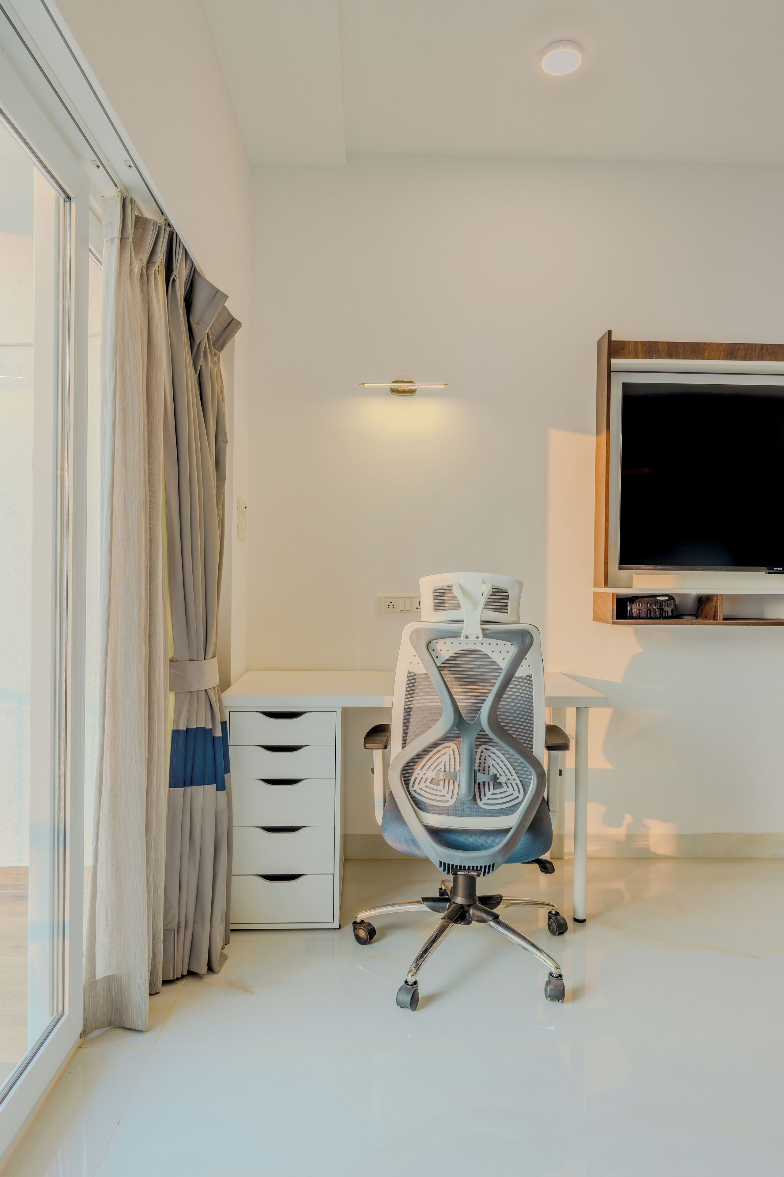 A modern office space with a desk, chair, and a large flat-screen TV.