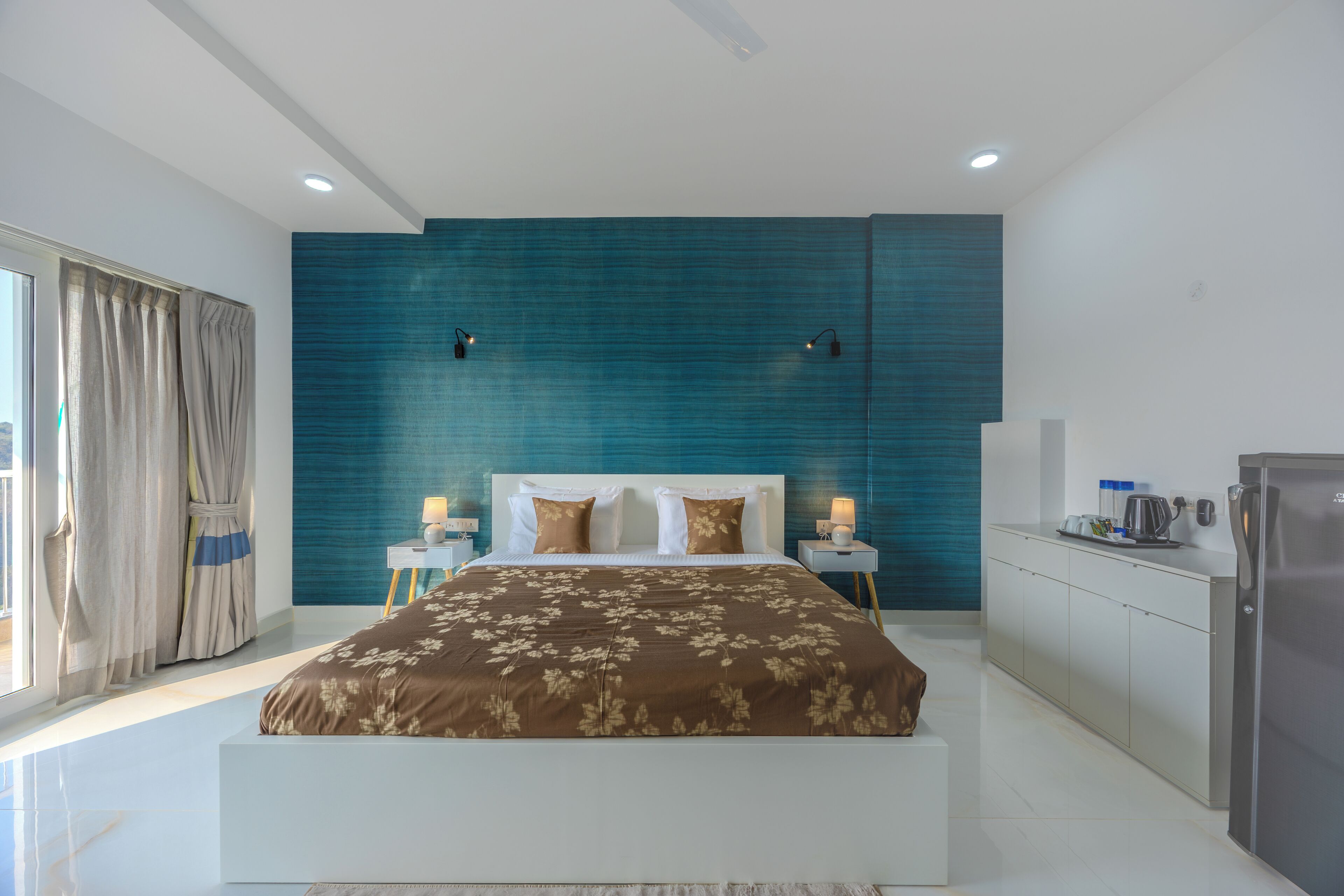 A modern bedroom with a large bed, a blue accent wall, and a kitchenette.