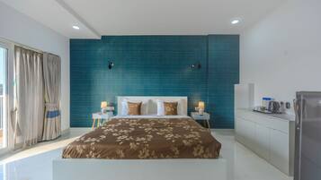 A modern bedroom with a large bed, a blue accent wall, and a kitchenette.