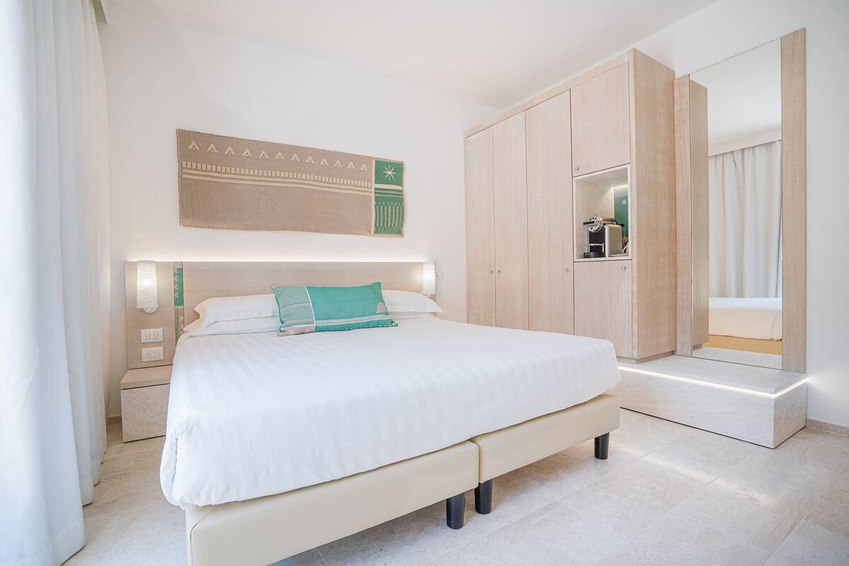 A modern bedroom with a large bed, a wardrobe, a bedside table, and a wall-mounted artwork.