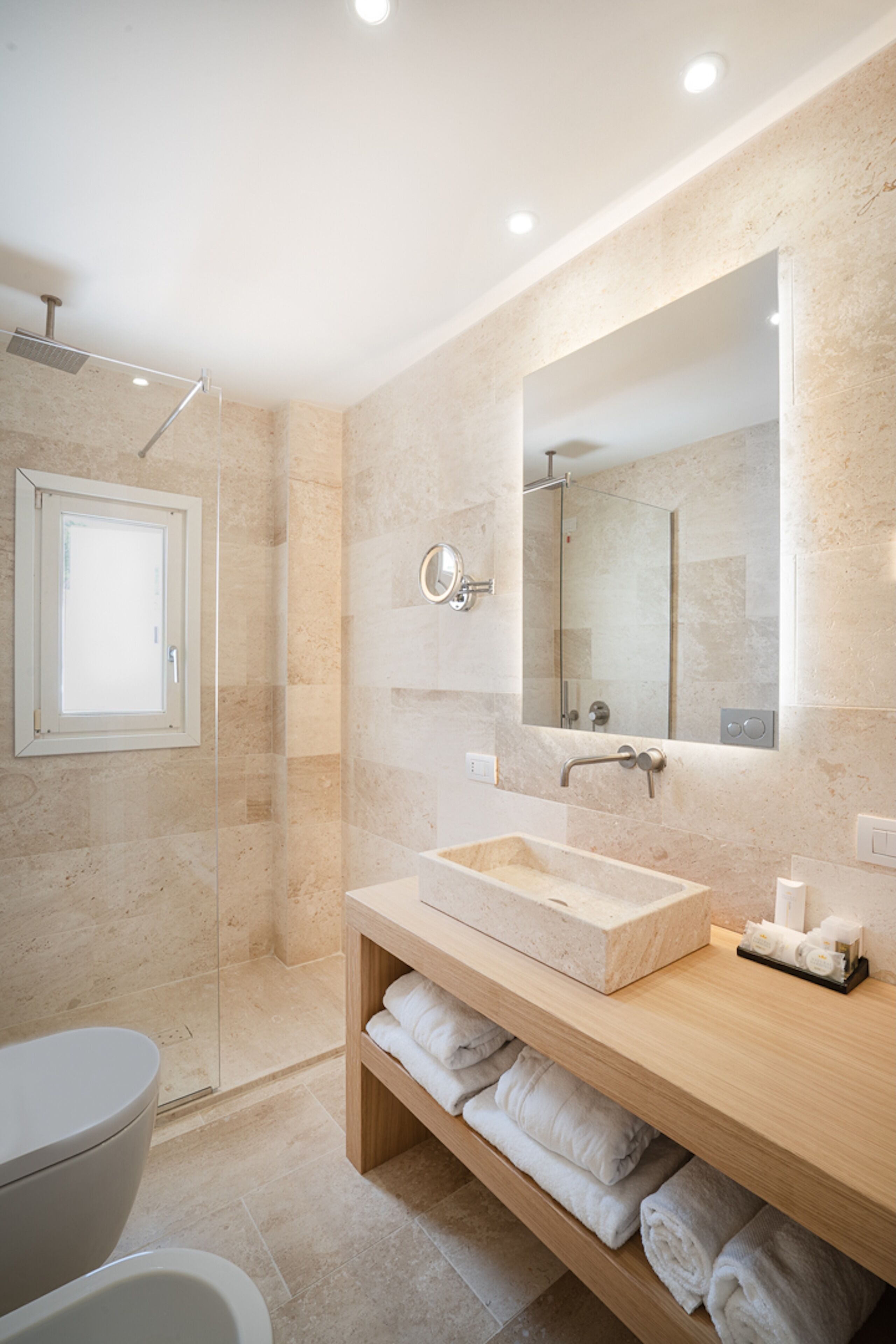 Un baño moderno con ducha acristalada, tocador de madera con lavabo color beige y un espejo grande.