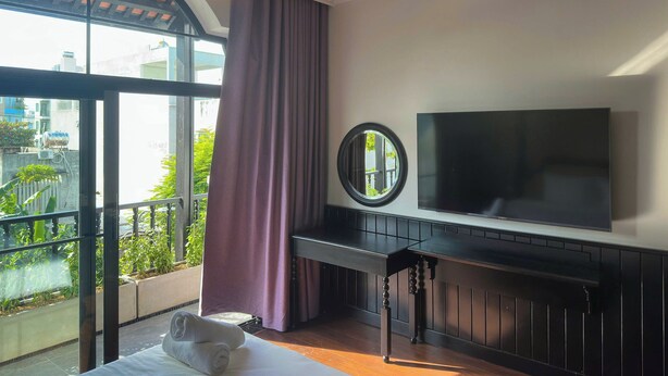 Una camera d'albergo con una grande finestra, una TV a schermo piatto fissata al muro, un letto con copriletto bianco e un piccolo tavolo con uno specchio.