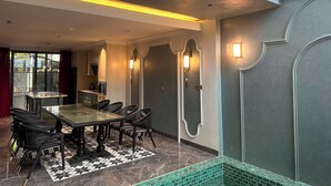 Zona pranzo con tavolo in vetro e sedie nere, tappeto decorato e vista su un balcone con ringhiera.
