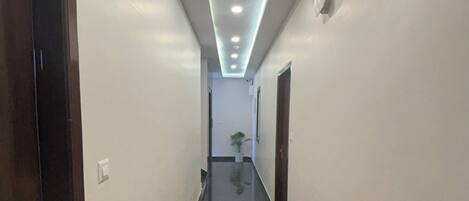 A long, narrow hallway with a shiny black floor, white walls, and recessed lighting.