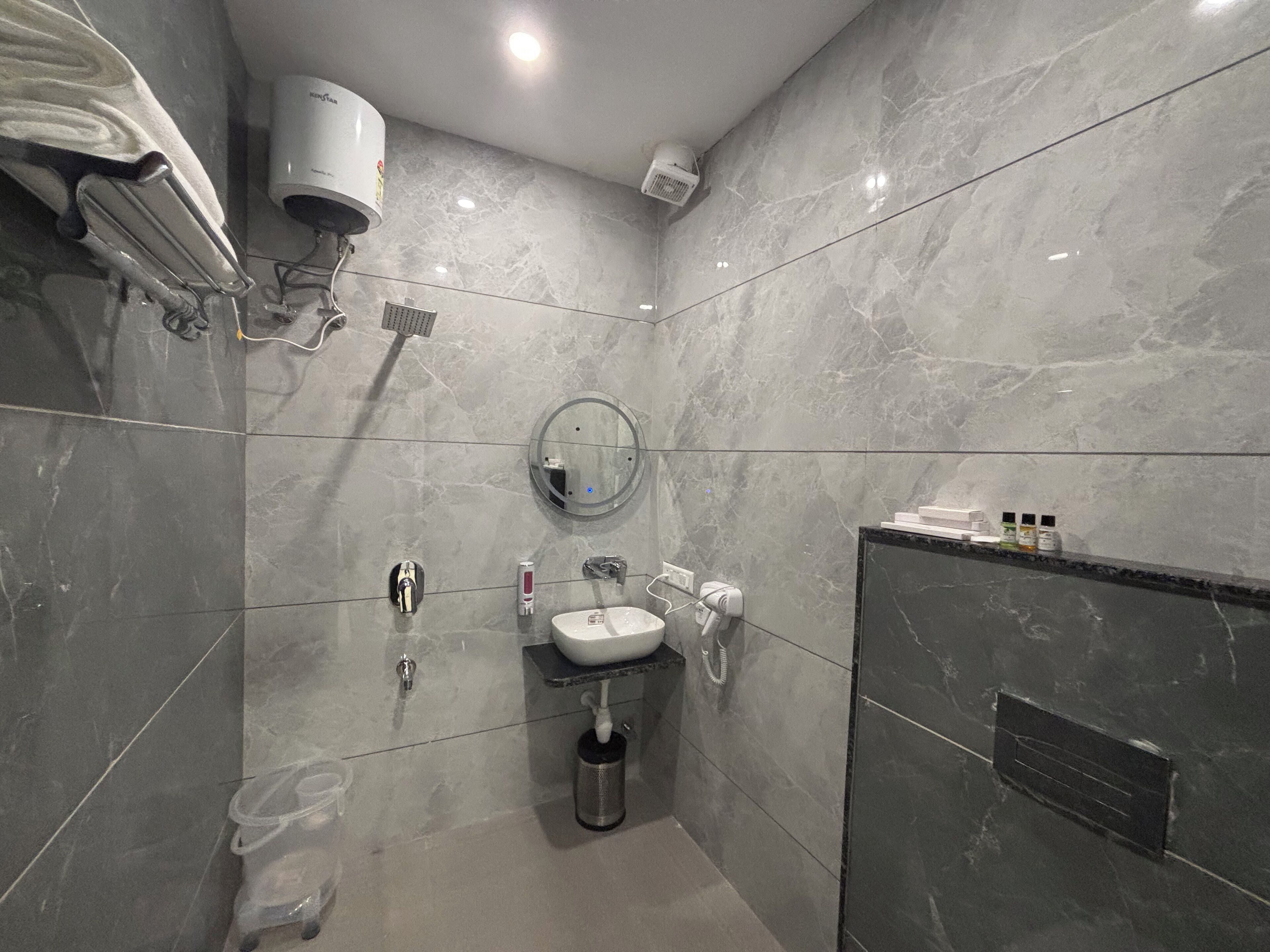 A modern bathroom with a marble wall, a built-in sink, a handheld showerhead, and a towel rack.