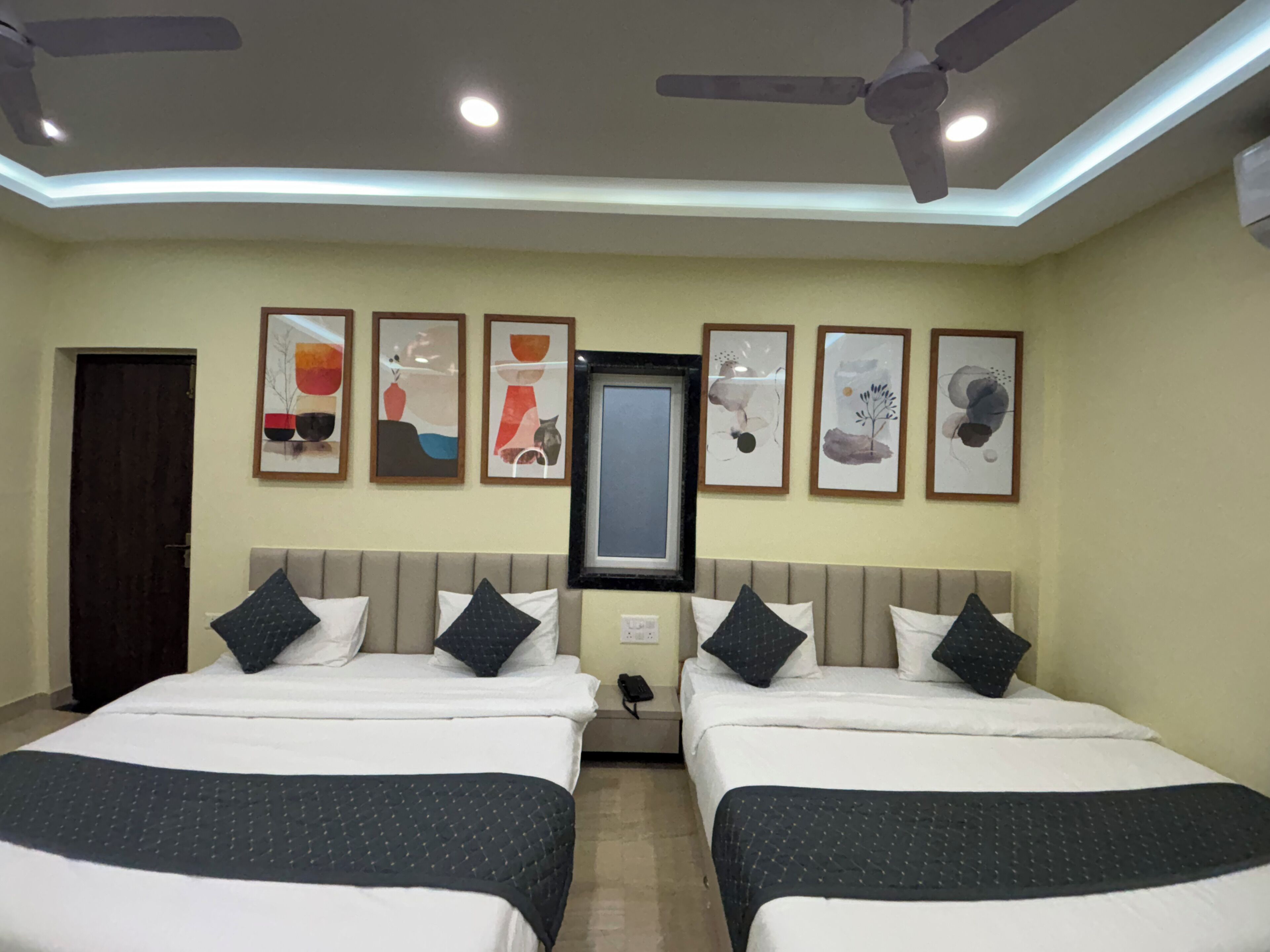 A hotel room with two beds, ceiling fans, recessed lighting, and abstract wall art.